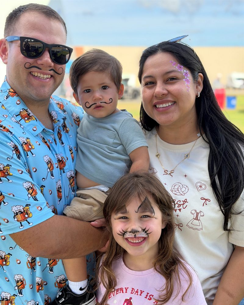 Smiling family with face-painted mustaches and flowers at an outdoor event